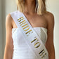 Model wearing white and gold bride to be sash