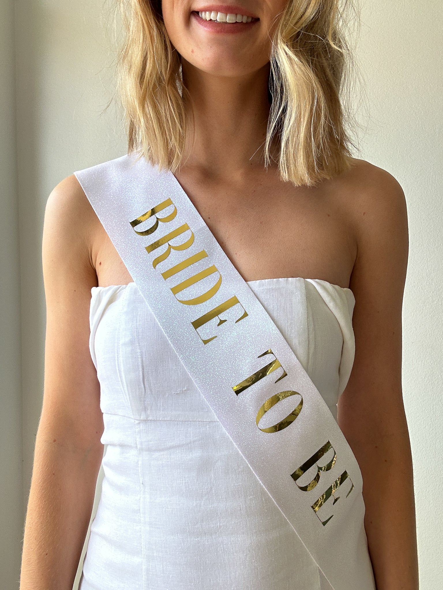 Model wearing white and gold bride to be sash